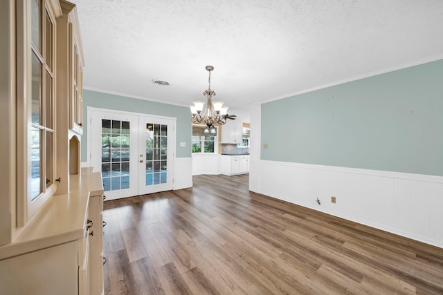 interior space featuring french doors, a textured ceiling, hardwood / wood-style flooring, a notable chandelier, and crown molding