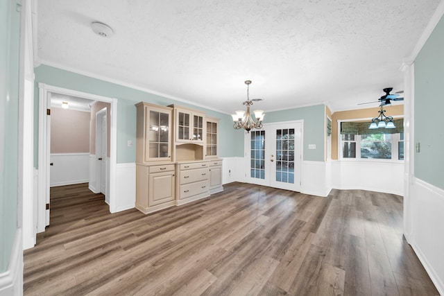 unfurnished dining area with ceiling fan with notable chandelier, crown molding, hardwood / wood-style flooring, and a textured ceiling