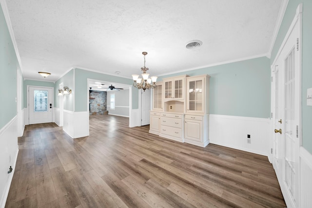 unfurnished dining area featuring wood-type flooring, a textured ceiling, ceiling fan with notable chandelier, and crown molding