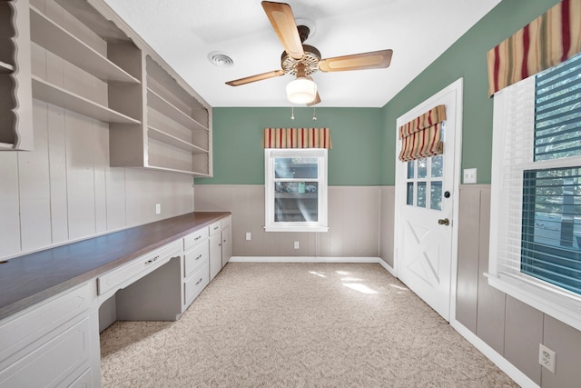 kitchen featuring ceiling fan, light colored carpet, and built in desk