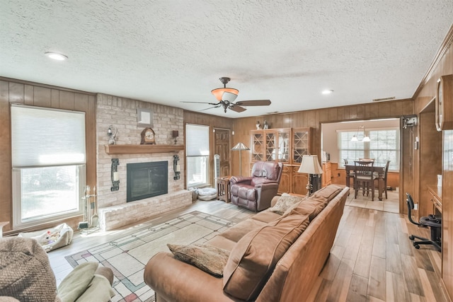 living area with a textured ceiling, wooden walls, visible vents, light wood-style floors, and a brick fireplace