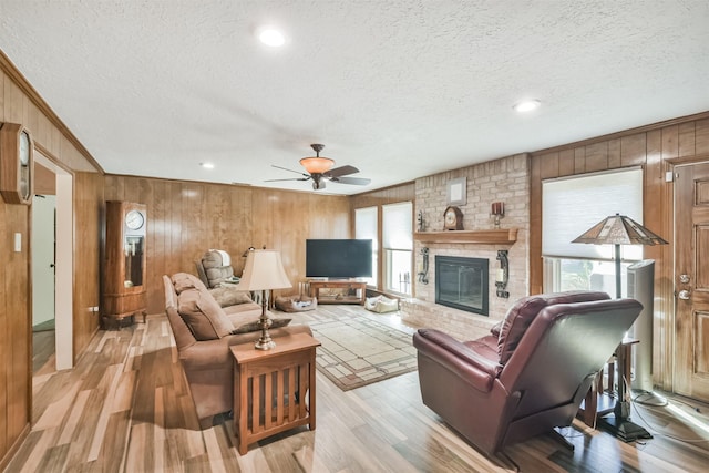 living area with ceiling fan, a textured ceiling, ornamental molding, a brick fireplace, and light wood finished floors