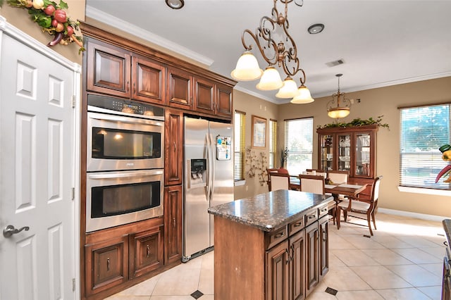 kitchen with appliances with stainless steel finishes, a kitchen island, hanging light fixtures, crown molding, and light tile patterned floors