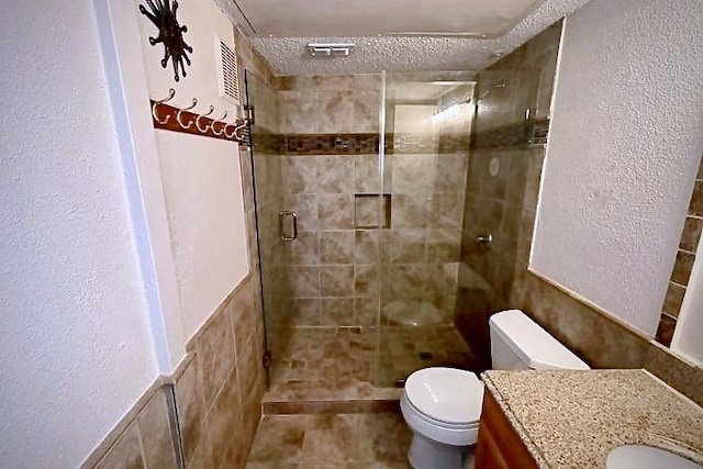 bathroom with vanity, a shower with door, toilet, and a textured ceiling