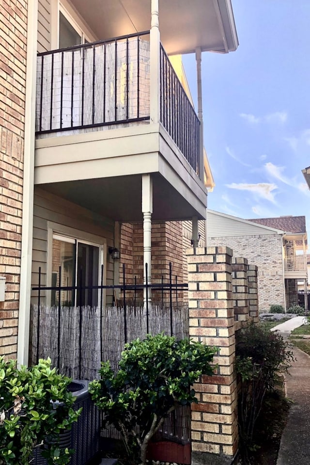 view of side of property with brick siding, fence, and a balcony