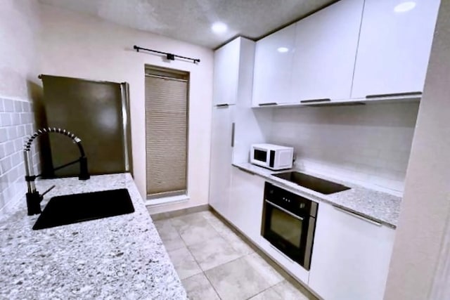 kitchen featuring black appliances, white cabinetry, sink, and light stone countertops