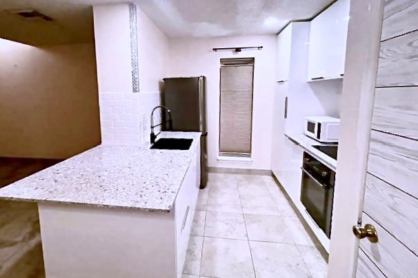 kitchen featuring oven, light stone counters, sink, white cabinets, and light tile patterned floors