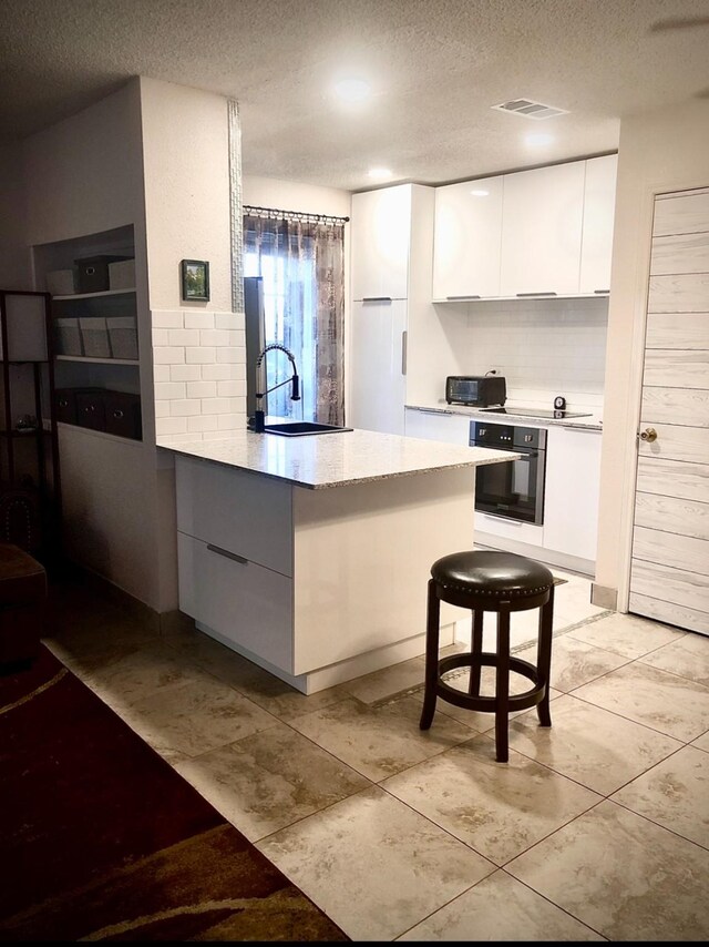 3600 Jeanetta St Unit 502, Houston, TX 77063 - kitchen with oven, modern cabinets, a sink, white cabinetry, and a textured ceiling