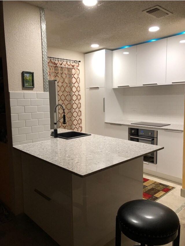 3600 Jeanetta St Unit 502, Houston, TX 77063 - kitchen featuring oven, a sink, black electric cooktop, white cabinetry, and tasteful backsplash