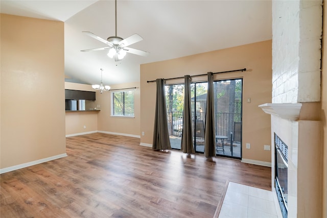 unfurnished living room with a large fireplace, wood-type flooring, ceiling fan with notable chandelier, and high vaulted ceiling