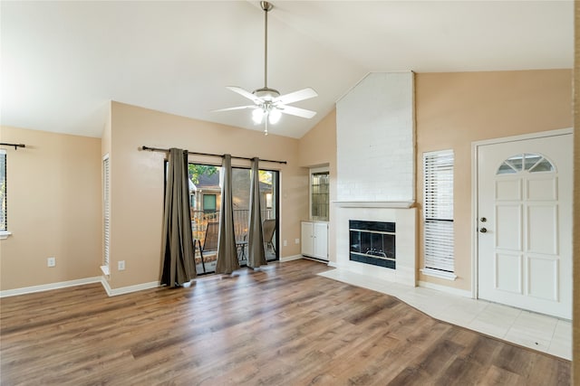 unfurnished living room with high vaulted ceiling, ceiling fan, a fireplace, and light hardwood / wood-style flooring