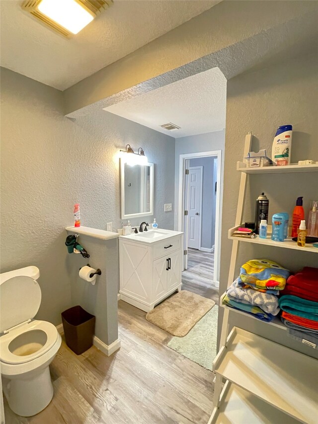 bathroom with hardwood / wood-style flooring, toilet, vanity, and a textured ceiling