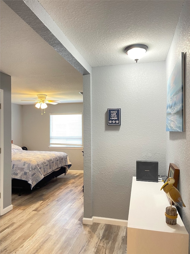 bedroom with light wood-type flooring, ceiling fan, and a textured ceiling