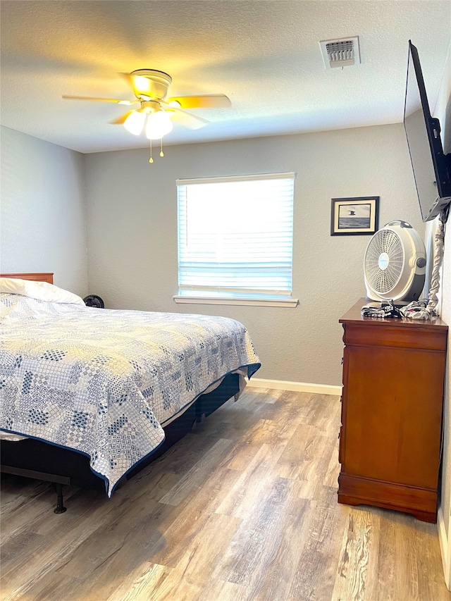 bedroom featuring light hardwood / wood-style floors, a textured ceiling, and ceiling fan