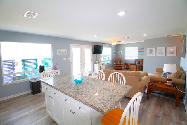 kitchen with ceiling fan, a kitchen island, light stone countertops, hardwood / wood-style flooring, and white cabinetry