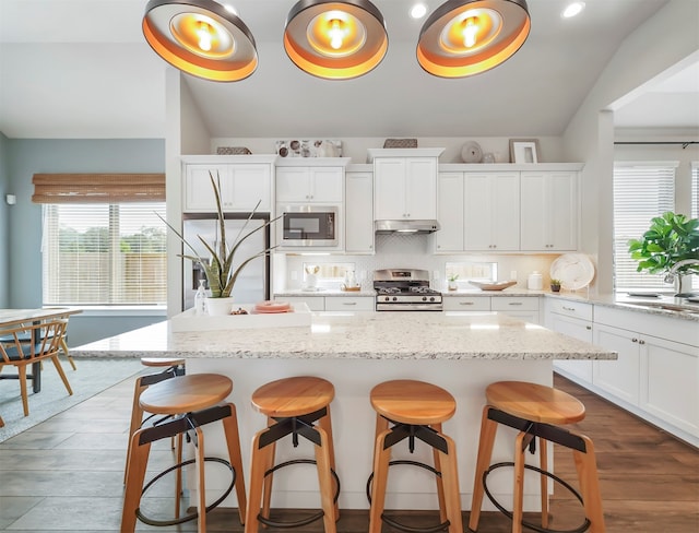 kitchen with a kitchen island, built in appliances, white cabinetry, and vaulted ceiling