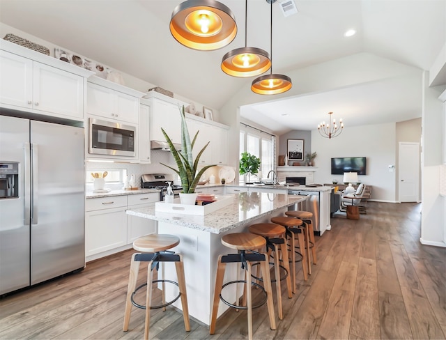 kitchen with stainless steel appliances, pendant lighting, vaulted ceiling, and white cabinetry