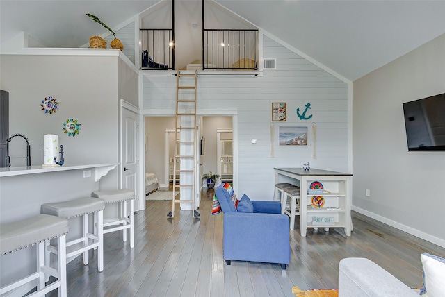 living room featuring hardwood / wood-style flooring, wood walls, sink, and high vaulted ceiling