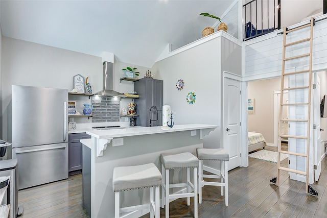 kitchen with light hardwood / wood-style flooring, ventilation hood, stainless steel refrigerator, a kitchen breakfast bar, and gray cabinets