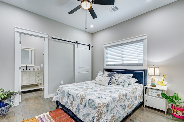 bedroom featuring ceiling fan, a barn door, connected bathroom, and light hardwood / wood-style floors