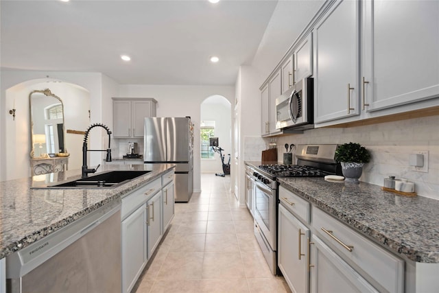 kitchen featuring light tile patterned flooring, stainless steel appliances, stone counters, and sink