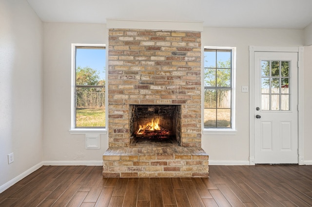 unfurnished living room featuring a healthy amount of sunlight, a brick fireplace, and dark wood-type flooring