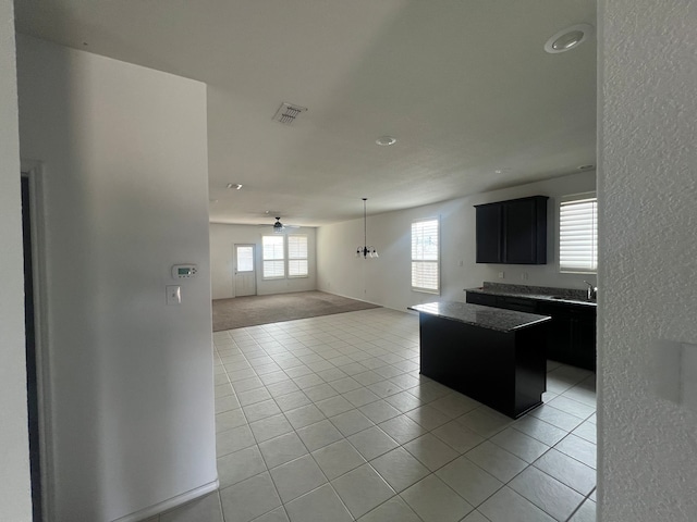 kitchen with light tile patterned flooring, ceiling fan with notable chandelier, sink, and a center island