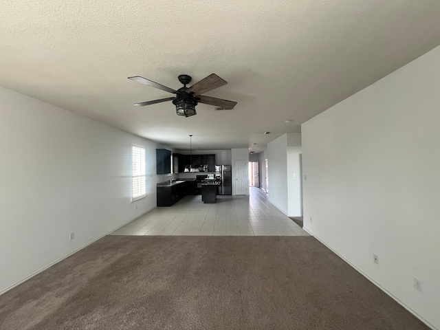 unfurnished living room with a textured ceiling, light colored carpet, and ceiling fan