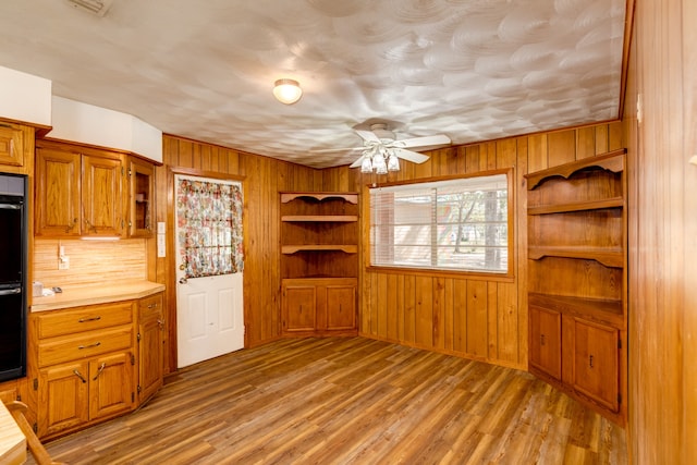 kitchen featuring black double oven, wooden walls, ceiling fan, and light hardwood / wood-style floors