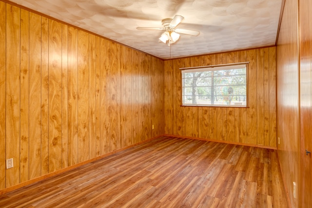 spare room with wood walls, wood-type flooring, and ceiling fan