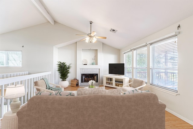 living room with ceiling fan, light hardwood / wood-style floors, a tile fireplace, and lofted ceiling with beams