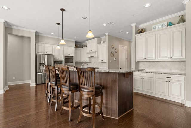 kitchen with appliances with stainless steel finishes, light stone countertops, hanging light fixtures, white cabinets, and a kitchen island with sink