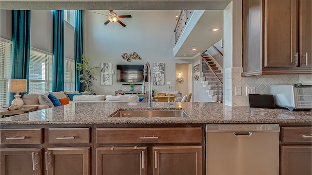 kitchen featuring ceiling fan, tasteful backsplash, sink, stone counters, and dishwasher