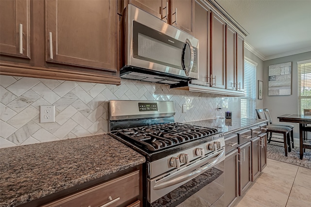 kitchen with ornamental molding, dark stone countertops, stainless steel appliances, and backsplash