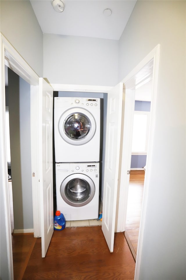 laundry room featuring stacked washer / dryer and dark wood-type flooring