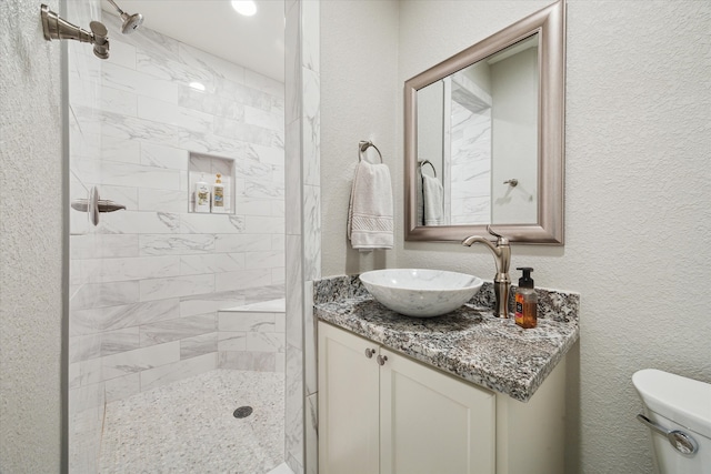 bathroom with a tile shower, vanity, and toilet