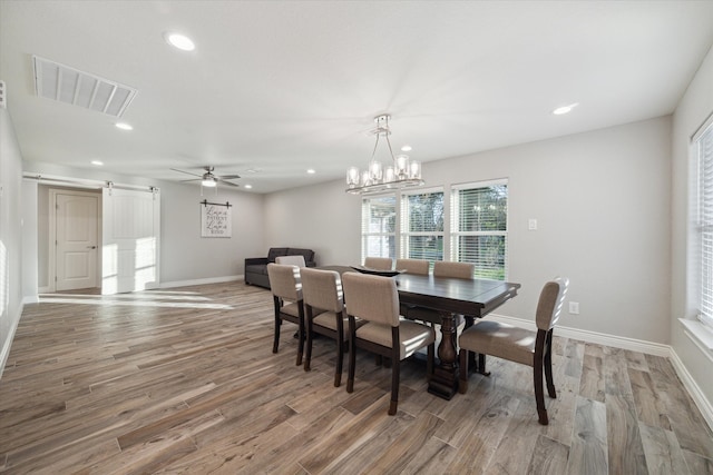 dining area with a barn door, wood-type flooring, and ceiling fan with notable chandelier