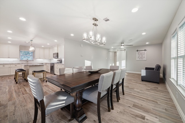 dining room with ceiling fan, a barn door, sink, and light hardwood / wood-style floors