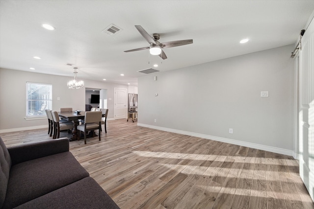 living room with ceiling fan with notable chandelier and light hardwood / wood-style floors