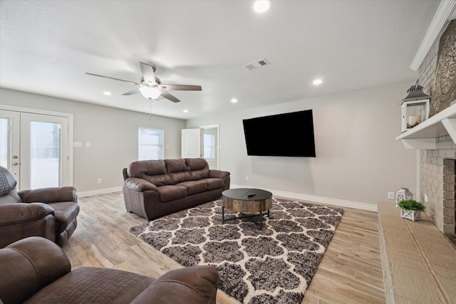 living room with a brick fireplace, light hardwood / wood-style floors, a textured ceiling, and ceiling fan