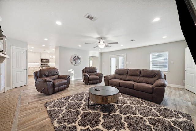 living room featuring ceiling fan with notable chandelier and light hardwood / wood-style flooring