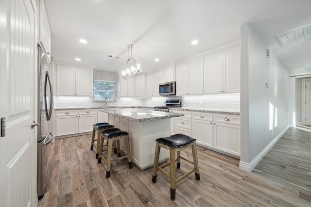 kitchen with decorative light fixtures, stainless steel appliances, white cabinetry, and a kitchen island