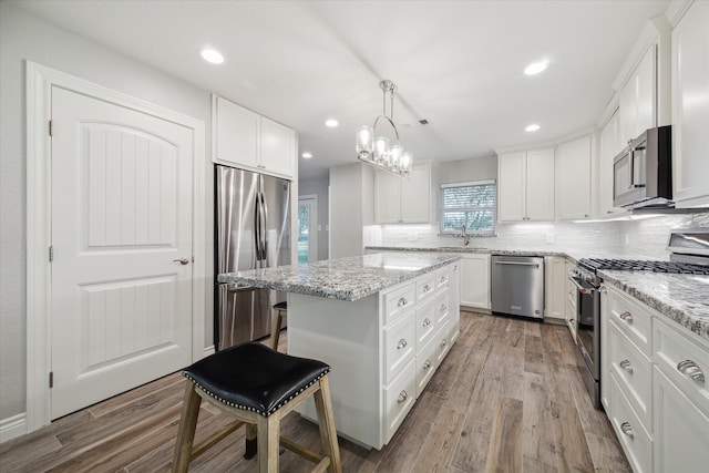 kitchen with a kitchen island, decorative light fixtures, white cabinetry, stainless steel appliances, and hardwood / wood-style floors