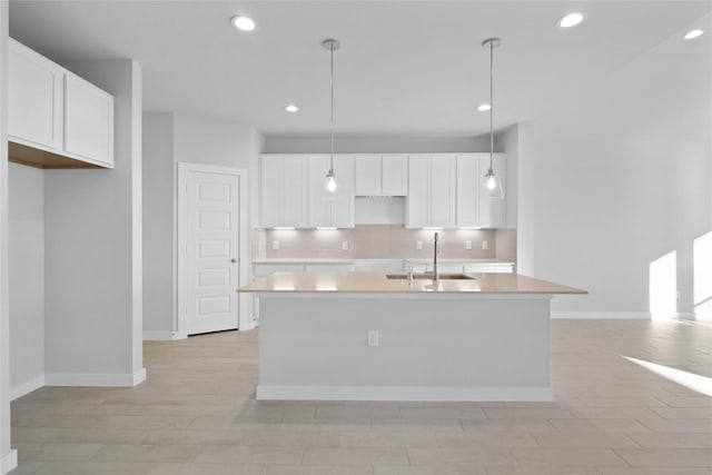 kitchen with white cabinetry, an island with sink, sink, and hanging light fixtures