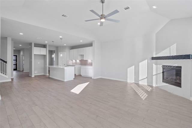 unfurnished living room with sink, vaulted ceiling, light hardwood / wood-style flooring, ceiling fan, and a tiled fireplace