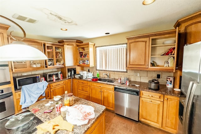 kitchen with appliances with stainless steel finishes, dark stone counters, sink, and backsplash