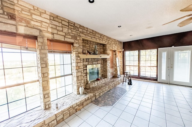 unfurnished living room featuring ceiling fan, a stone fireplace, a textured ceiling, and light tile patterned floors