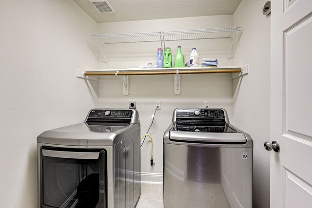 laundry area with a textured ceiling, light tile patterned flooring, and washing machine and clothes dryer