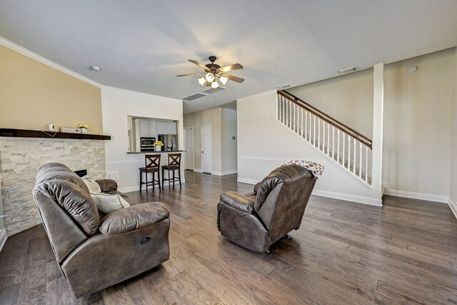 living room featuring ornamental molding, a stone fireplace, ceiling fan, and dark hardwood / wood-style flooring