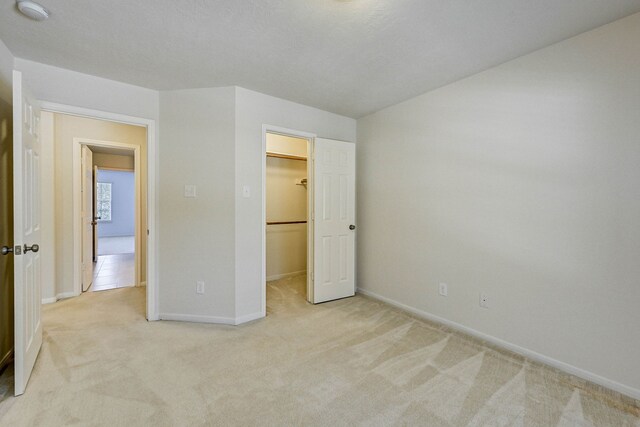 unfurnished bedroom with light colored carpet, a closet, and a walk in closet